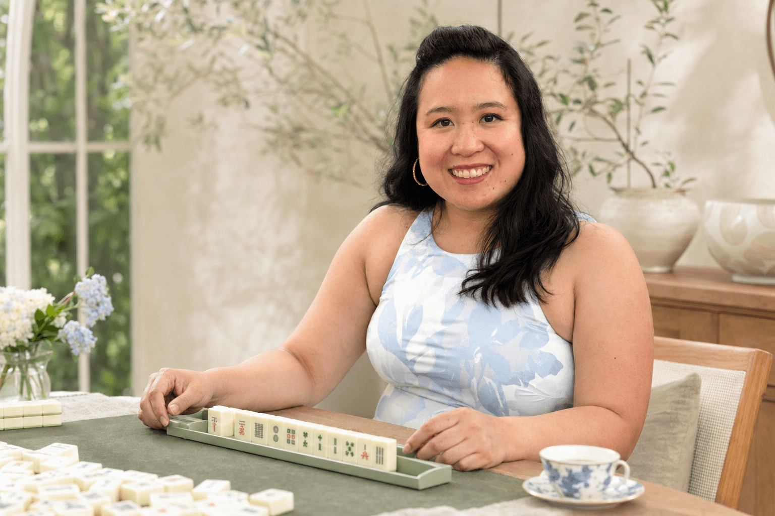 Christine smiling at a Mahjong table in a sunlit room.